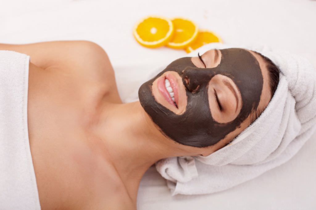 Beautiful young woman is getting facial chocolate mask at spa. She is lying with closed eyes. The girl is smiling